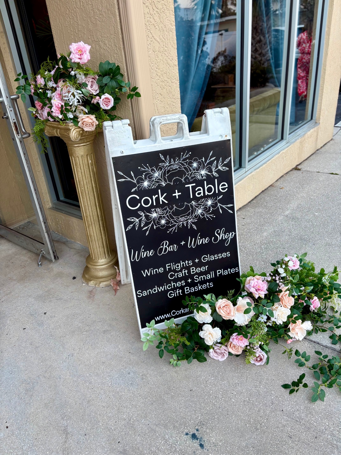 The Cork + Table sidewalk sign with floral arrangements at the storefront